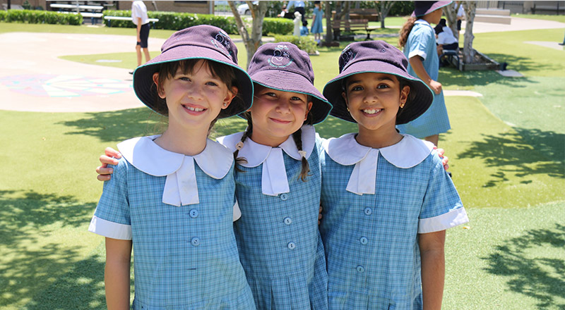 Students in their summer uniform at Older student reading together with a younger student in the playground at Our Lady of the Angels Primary School Rouse Hill