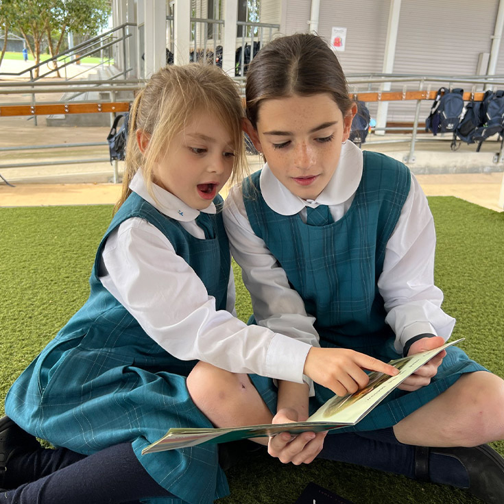 Older student reading together with a younger student in the playground at Our Lady of the Angels Primary School Rouse Hill