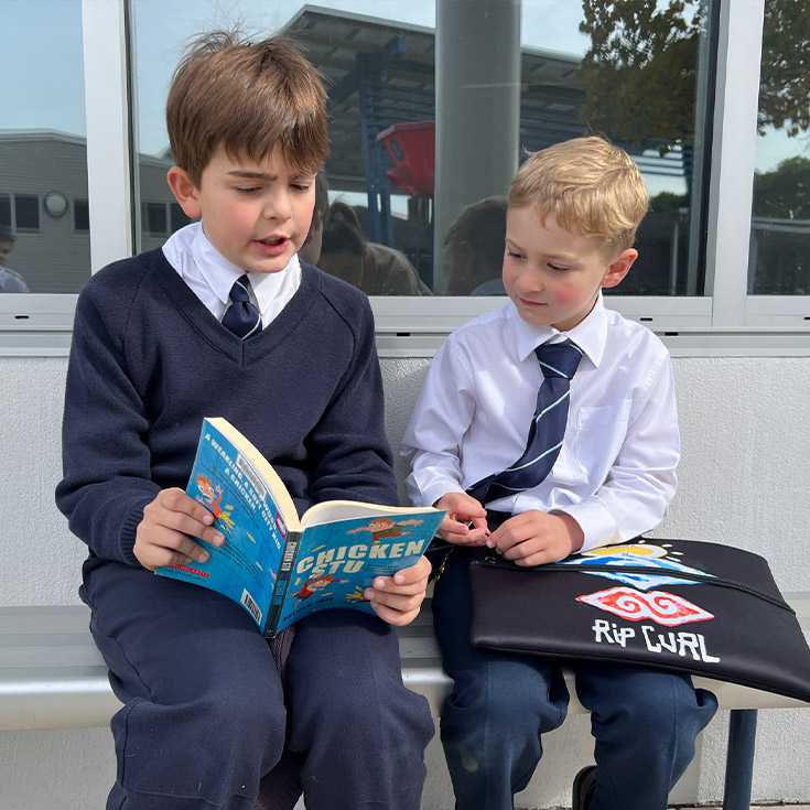 Older student reading together with a younger student in the playground at Our Lady of the Angels Primary School Rouse Hill