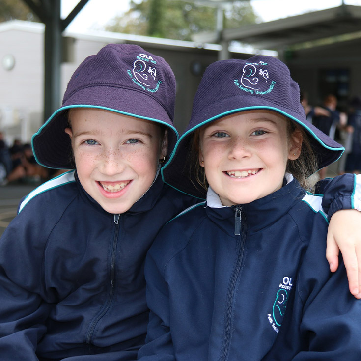 Students smiling together in the playground at Older student reading together with a younger student in the playground at Our Lady of the Angels Primary School Rouse Hill