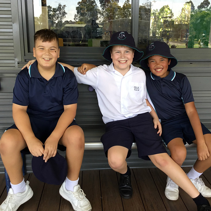 Students with their arms around eachother in the school playground at Older student reading together with a younger student in the playground at Our Lady of the Angels Primary School Rouse Hill